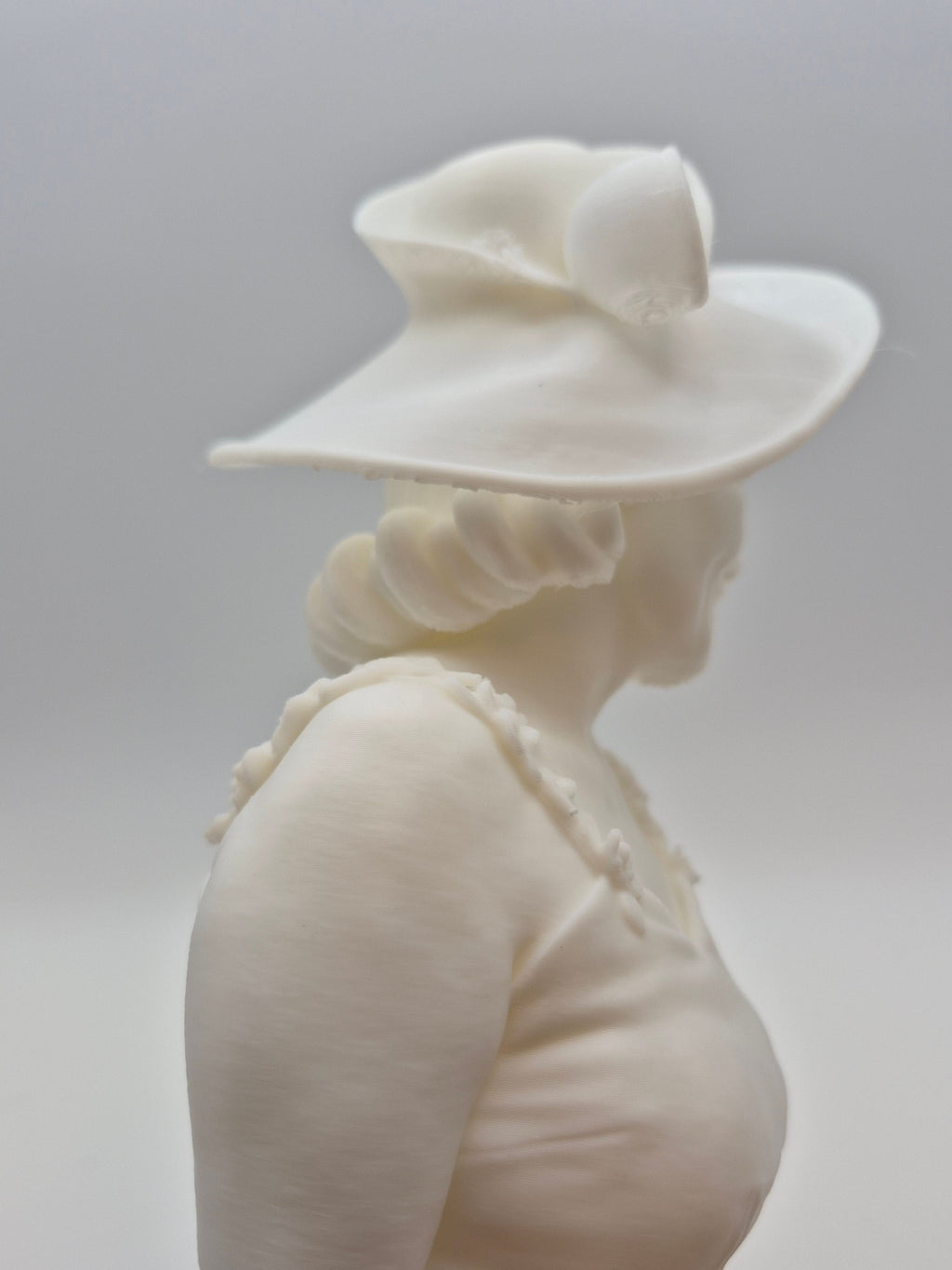 White ceramic sculpture of a person wearing a hat on a plain background